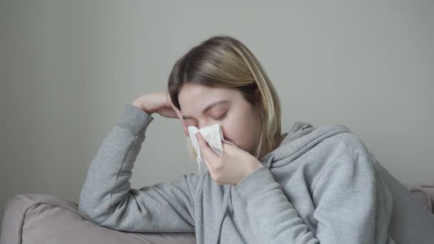 Primer plano. La chica rubia con el pelo corto está enferma, estornuda y se envuelve en una manta de la temperatura. Síntoma de Orvi, coronovirus, enfermedad respiratoria aguda, alergia, sinusitis . — Vídeo de stock