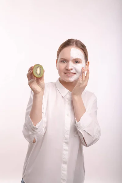 Ragazza con una maschera bianca sul viso. Tenendo il kiwi di frutto . — Foto Stock