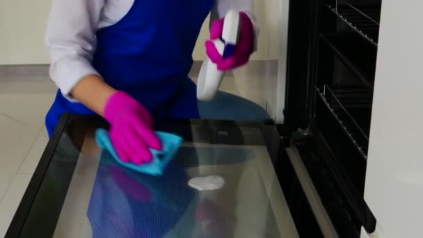 Primer plano de una hermosa niña limpia el horno con un detergente en guantes de color rosa para la limpieza. Vista frontal . — Vídeo de stock