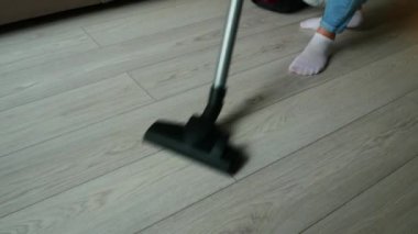 Mavi kotlu bir kızın kırpılmış görüntüsü. Yerlerin ahşap yüzeyini temizliyor, süpürüyor.