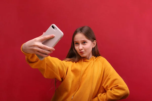 Uma linda menina tira uma selfie em seu telefone celular . — Fotografia de Stock