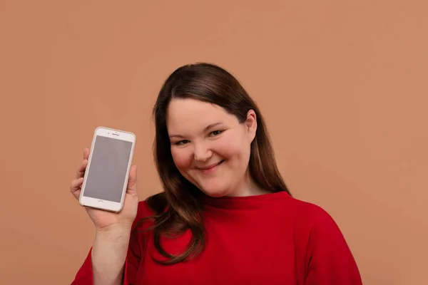 Una hermosa chica con sobrepeso muestra su teléfono móvil. Con una pantalla vacía . — Foto de Stock