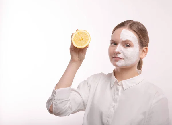 Schöne junge Mädchen mit Sahne im Gesicht. Weißes Hemd und weißer Hintergrund. — Stockfoto