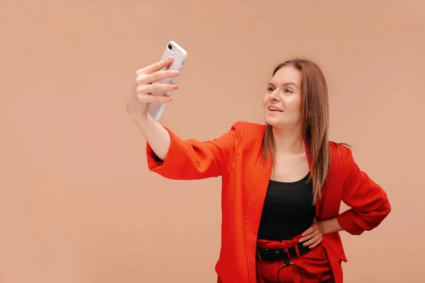 Una hermosa chica en ropa brillante toma una selfie en su teléfono inteligente . — Foto de Stock