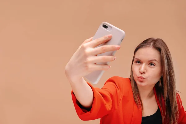 Una hermosa chica en ropa brillante toma una selfie en su teléfono inteligente. beso de aire . — Foto de Stock