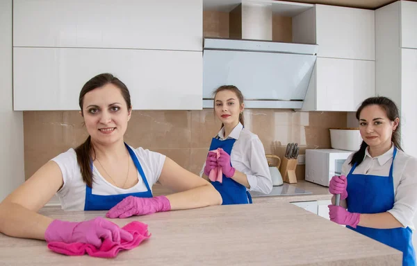 Een team van mooie jonge meisjes die het huis schoonmaken. Witte heldere keuken. — Stockfoto