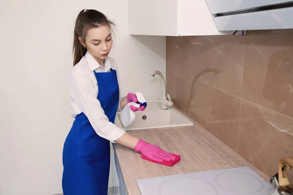 Giovane bella ragazza lava una stufa elettrica con detergente con uno spray . — Foto Stock