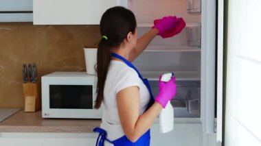 Genç ve güzel bir kadın sırtüstü duruyor, beyaz bir buzdolabı açıyor ve rafları yıkıyor..