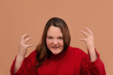 Bej arka planda izole edilmiş öfkeli genç bir kadın görüntüsü.