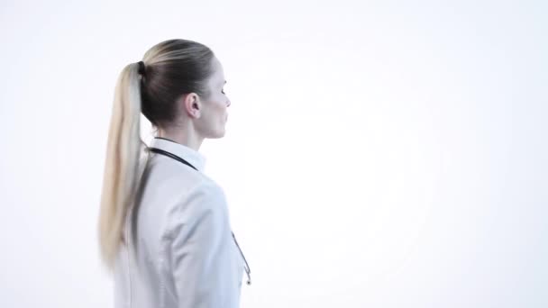 Een blond meisje staat met haar rug in een wit gewaad en draait haar gezicht. — Stockvideo