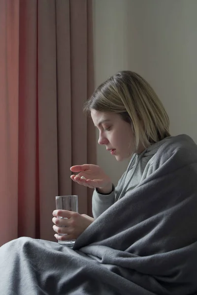 Zieke jonge vrouwen die pillen nemen terwijl ze op de bank zitten — Stockfoto