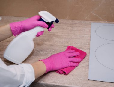 Beyaz bir mutfakta elektrikli sobayı beyaz bir kavanozda sprey ve mikrofiber bezle temizlemek..