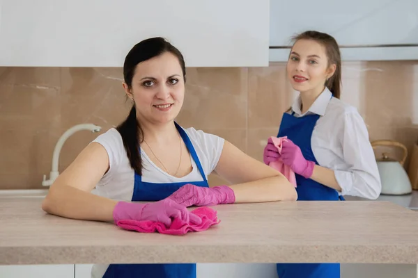 A team of beautiful young girls doing house cleaning. Girl in white shirts. White bright kitchen. — Stock Photo, Image