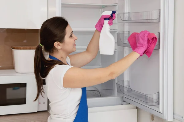 A woman in pink gloves washes a white refrigerator.