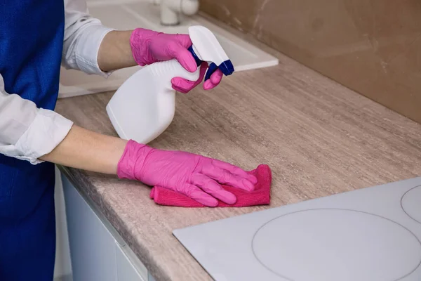 Uma menina em luvas de borracha rosa lava uma superfície do armário com um pano de microfibra . — Fotografia de Stock