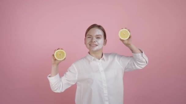Veselá dívka drží dva citróny v rukou, bílý přírodní krém je aplikován na její obličej.