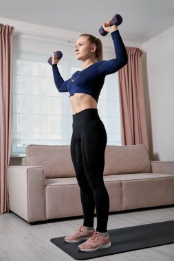 Sağlıklı bir yaşam tarzı. Genç ve güzel bir kız evde halterlerle egzersiz yapıyor..