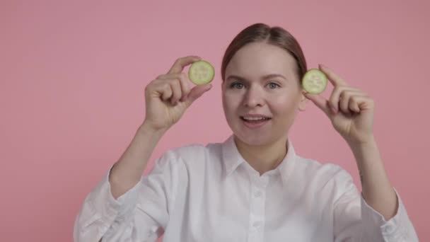 Begreppet naturliga kosmetika. En ung flicka utan smink håller i sina händer två skivor gurka nära ögonen. — Stockvideo