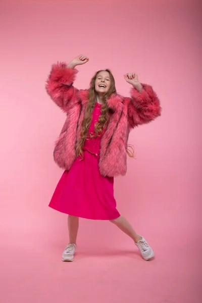 Menina bonita em um casaco de pele elegante com pele rosa, um vestido rosa e sapatos de ginástica branca está dançando . — Fotografia de Stock