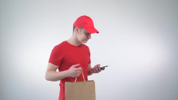 Mladík kurýr mluví na mobilu s klientem a upřesňuje adresu. — Stock video