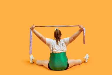 Sırtı elinde kurdeleyle oturan şişman bir kız. Spor yapmak.