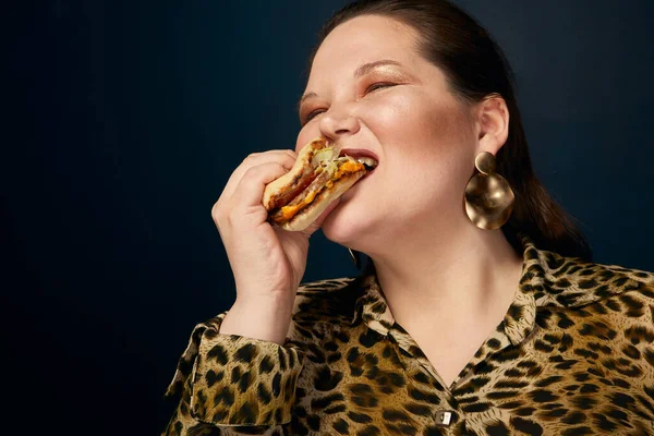 Koncept nenasytnosti. Nadváha. Tlustá žena v leopardí tiskové blůze s hamburgerem v ruce. — Stock fotografie