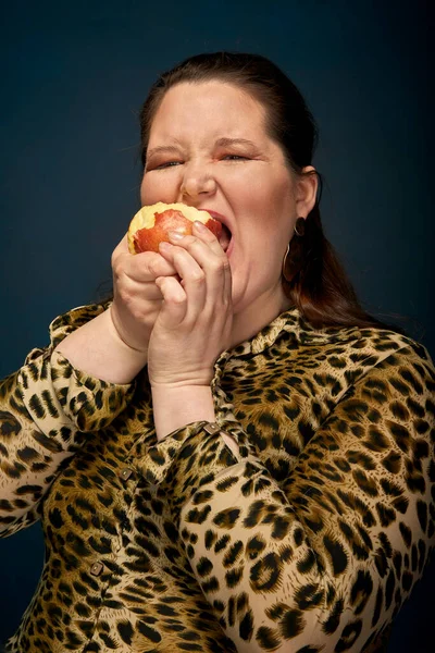 Hladová tlustá holka jí červené jablko. správné výživy. Tmavě modré pozadí. — Stock fotografie