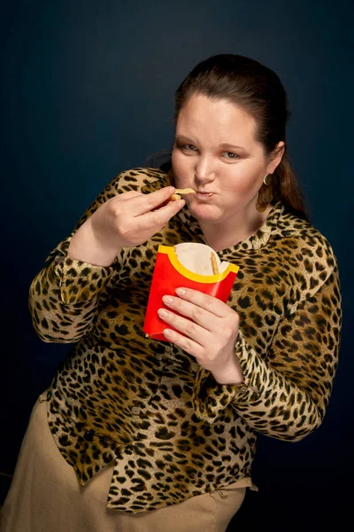 Gruba dziewczyna patrzy w kamerę i je frytki z wielkim apetytem. Szybkie żarcie. Koncepcja obżarstwa. — Zdjęcie stockowe