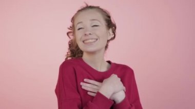 Dalgalı saçlı mutlu bir kız ellerini göğsüne koyar..