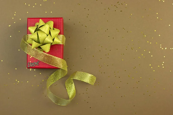 Holiday gift in a red box and with a gold ribbon and sparkles on a brown background, holiday concept, place for text