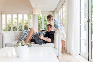 Çift, lüks villada dizüstü bilgisayarlarıyla kanepede dinleniyor.