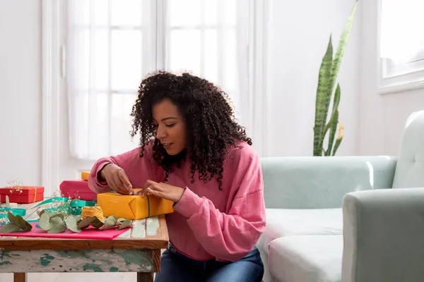 Mujer latina envolviendo regalos artesanales hechos a mano en la mesa en casa — Foto de Stock