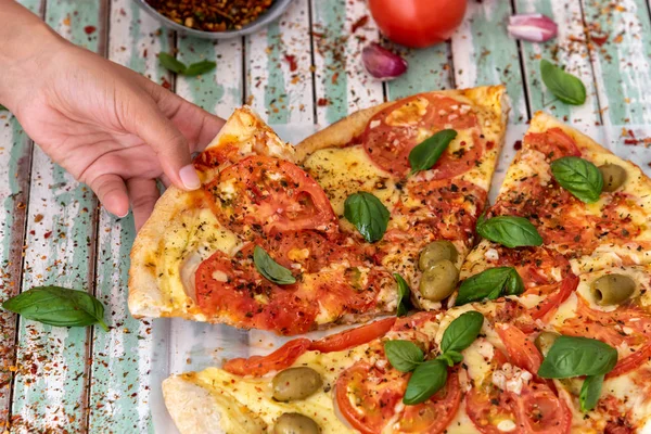 Yukarıdan bakıldığında kırsal turkuaz tahtalardan bir dilim pizza alan bir kadının eli.