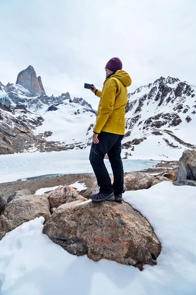 A hiker with a yellow jacket taking a photo on the base of Fitz Roy Mountain in Patagonia, Argentina — Stock Photo, Image