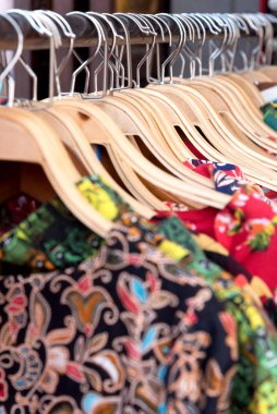 Bir mağazadaki raftan farklı renklerde kıyafetler sarkıyor.