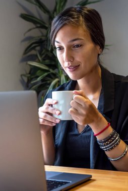 Evde dizüstü bilgisayar ve belgelerle çalışan genç bir kadın.