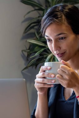 Evde dizüstü bilgisayar ve belgelerle çalışan genç bir kadın.