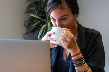 Evde dizüstü bilgisayar ve belgelerle çalışan genç bir kadın.