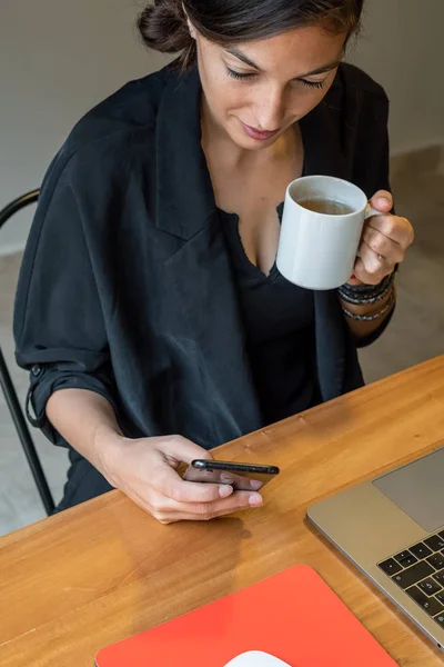 Young woman working at home with laptop and texting on the phone