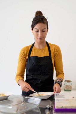 Önlüklü genç bir kadın modern bir mutfakta kahvaltı için omlet pişiriyor.