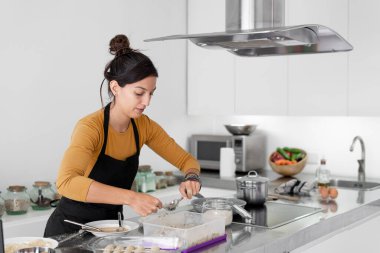 Önlüklü esmer kadın modern bir mutfakta ev yapımı kroket pişiriyor.