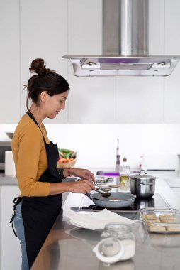 Genç esmer kadın evde yemek pişiriyor.