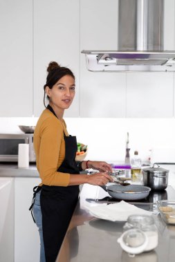 Genç esmer kadın evde yemek pişiriyor.