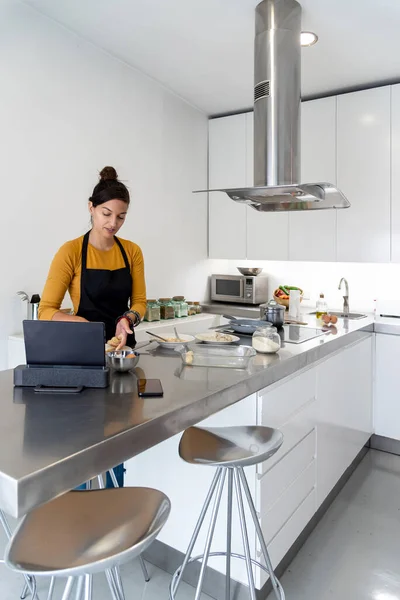 Brunette woman cooking a recipe from a digital tablet in a modern kitchen