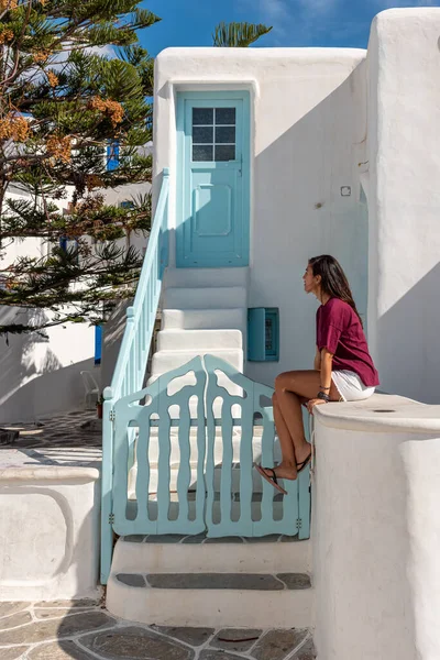 ギリシャの青い木製のドアの前に座って赤いTシャツの女性 — ストック写真