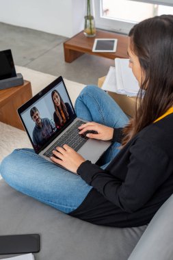 Bilgisayarı ve tableti olan genç bir kadın evinde iş telekonferansı yapıyor.