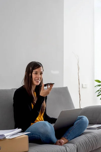 Young woman with laptop and phone telecommuting on the sofa at her home