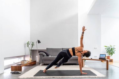 Fit Kadın tabletindeki online eğitim programını kullanarak minderinde yoga yapıyor.