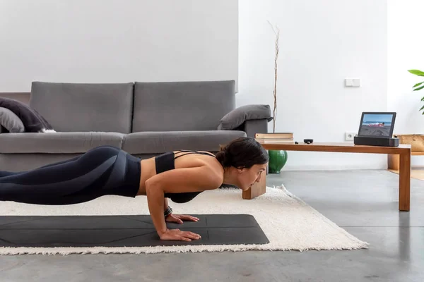 Chaturanga çalışan sağlıklı kadın evdeki tabletteki yoga programını kullanarak poz veriyor.