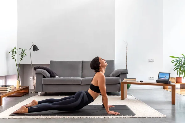 Kobra pozu veren formda bir kadın evdeki tabletteki yoga programını kullanıyor.